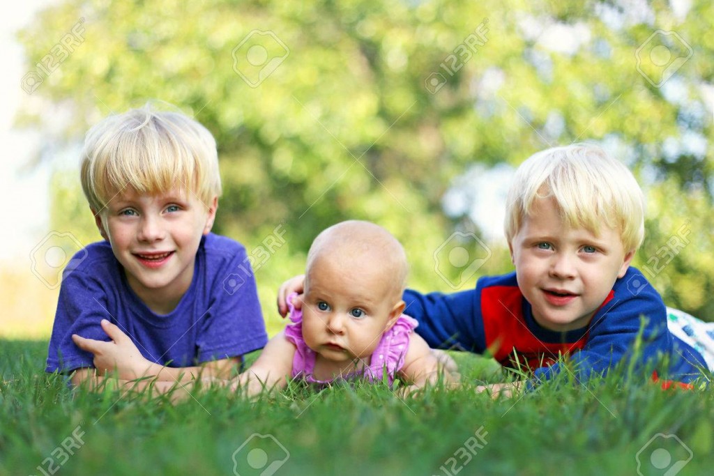 Portrait of Three happy young siblings: a young child, his little brother and their baby girl sister are laying outside in the grass on a summer day.